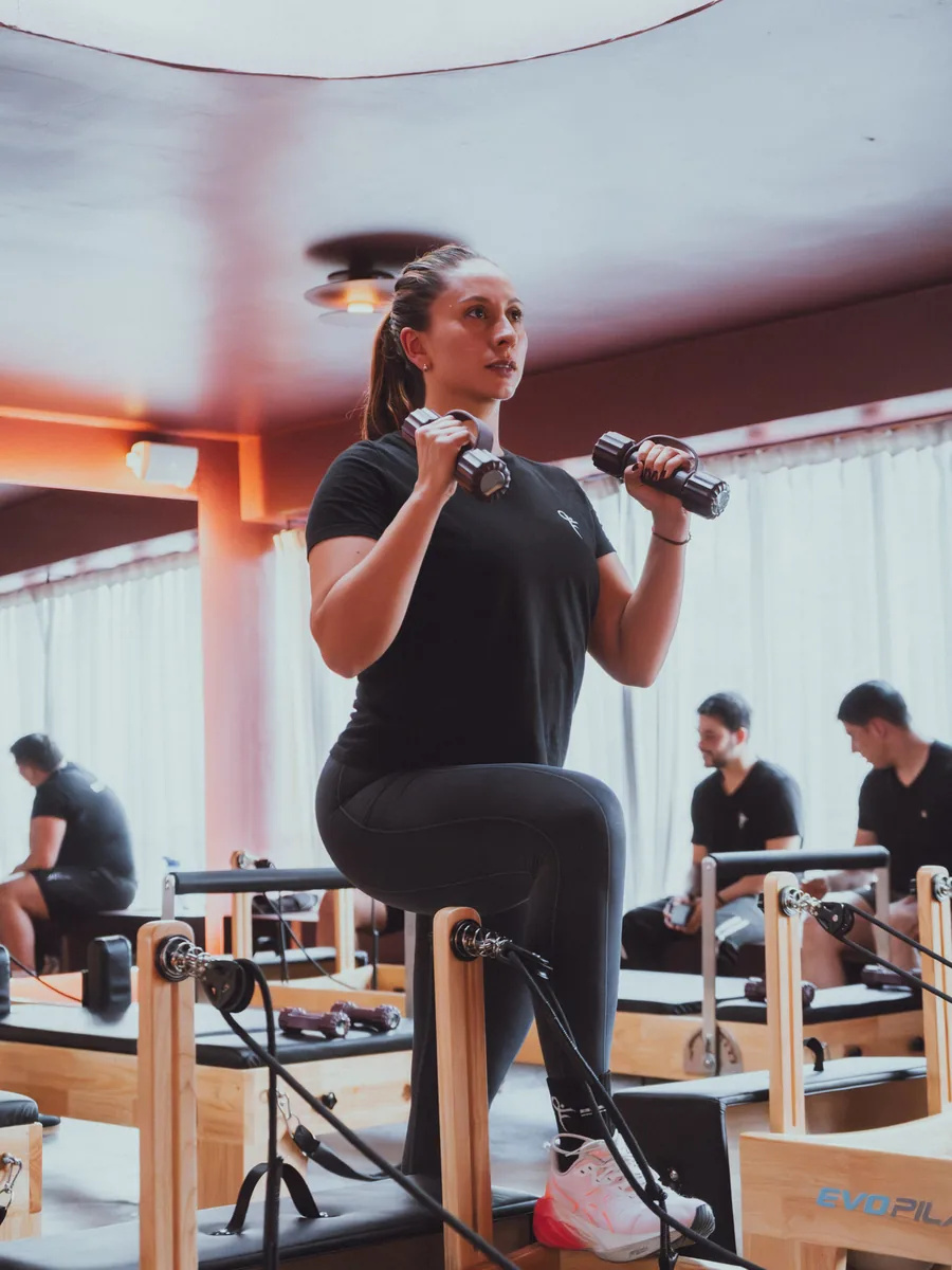 La misma entrenadora haciendo un ejercicio de fuerza con mancuernas en la sala.